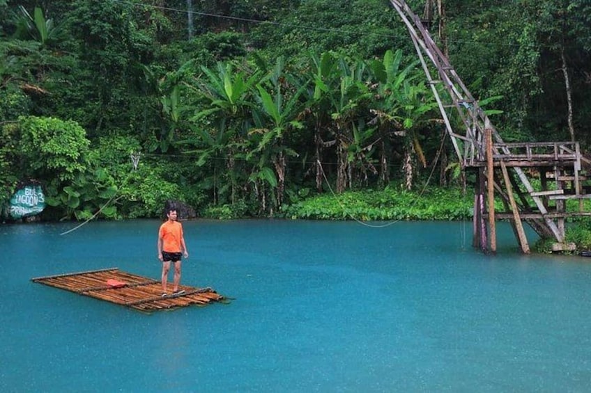 A person standing on a floating platform in a body of water, surrounded by lush greenery and a wooden structure. 2