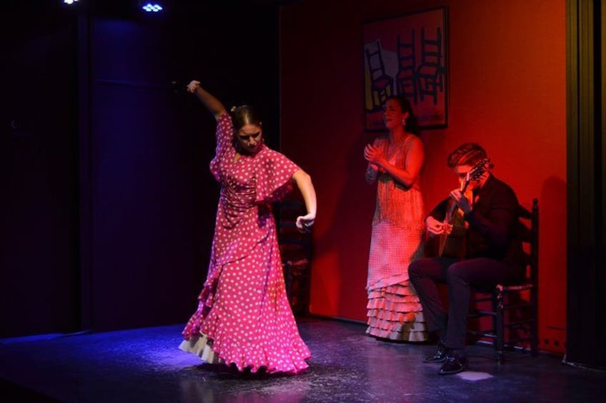 A stage with a person in a pink polka dot dress dancing, another person in a white dress clapping, and a person playing a guitar. 4