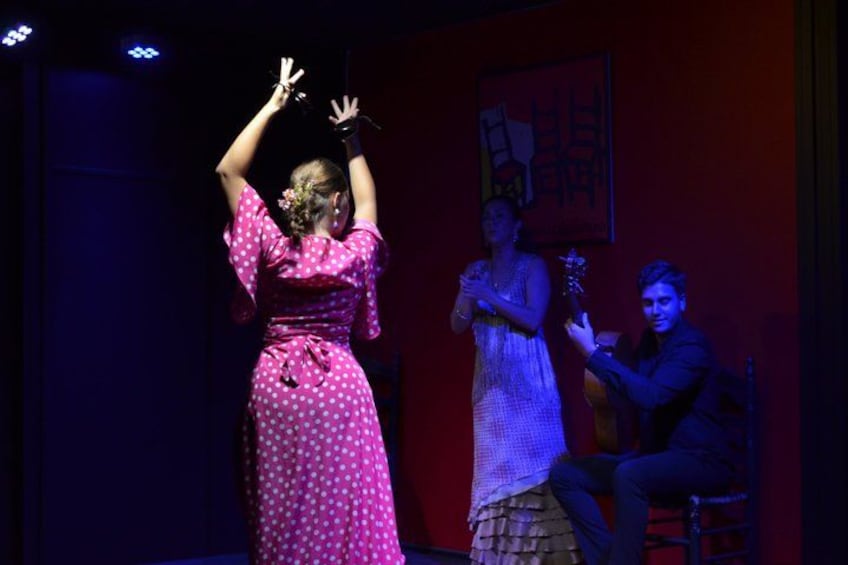 A person in a pink polka dot dress performing on stage with another person in a white dress in the background. 2