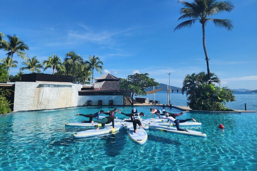 People on paddleboards in a pool surrounded by palm trees and a clear sky. 1