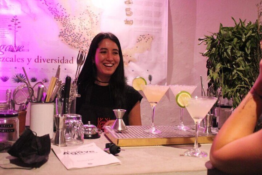 A bar setting with a bartender, a cocktail menu, and a plant in the background. 1