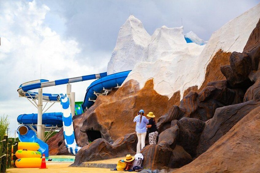 A water park with a blue water slide, rocky terrain, and a person with a backpack. 4