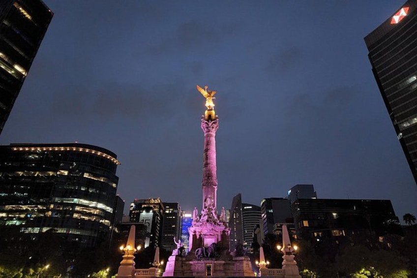Une vue nocturne d’une ville, avec des bâtiments illuminés et une statue imposante au centre. 5