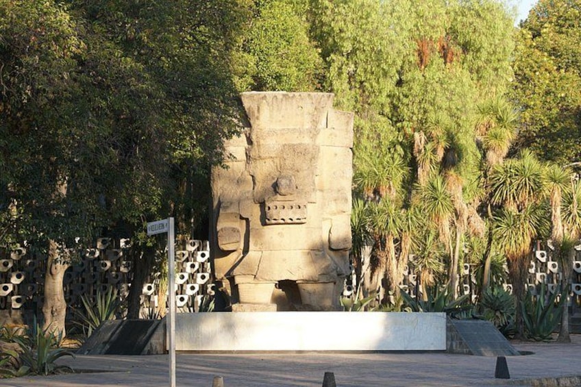 Une grande sculpture en pierre représentant un visage, entourée d’arbres et de plantes. 4