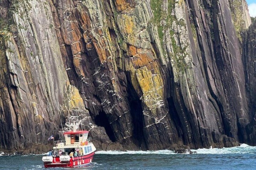 A boat navigating near a large, rugged cliff. 1