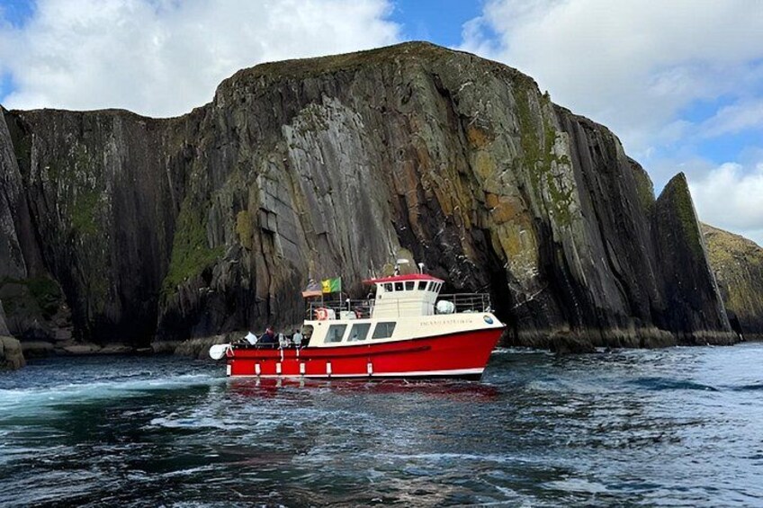 A red and white boat on water with a large rocky cliff in the background. 1