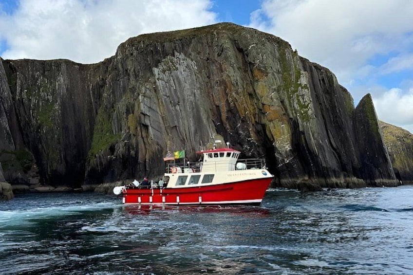A red and white boat navigating near a large, rugged cliff. 1