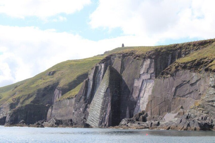 A coastal cliff with a prominent vertical rock face and a small structure on top. 3