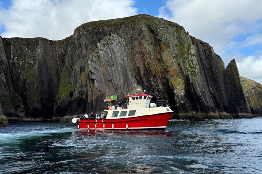 A red and white boat on water with a large rocky cliff in the background. 1