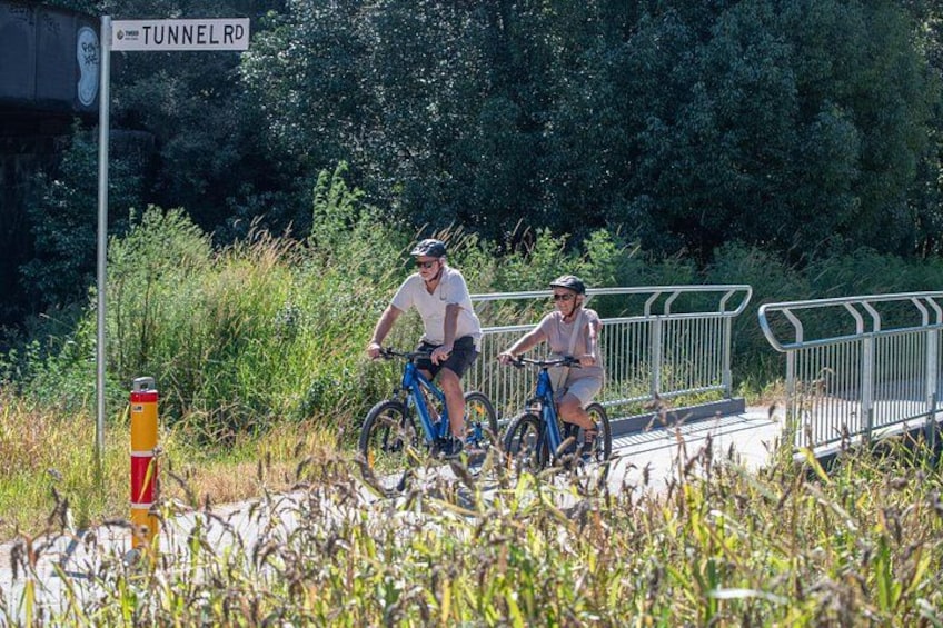 Two cyclists on a paved path with a sign reading 'TUNNEL RD' and a red and yellow traffic cone. 3