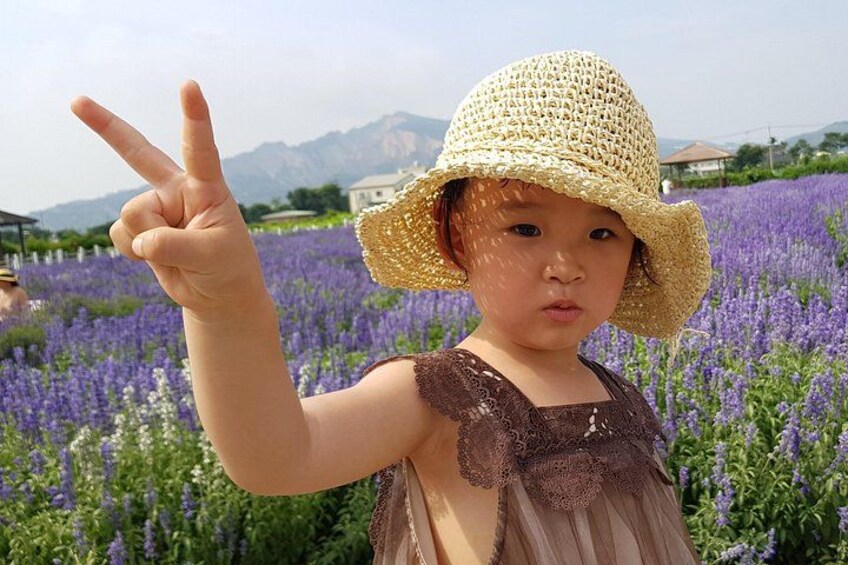 A child in a field of purple flowers, wearing a straw hat and a brown dress. 4