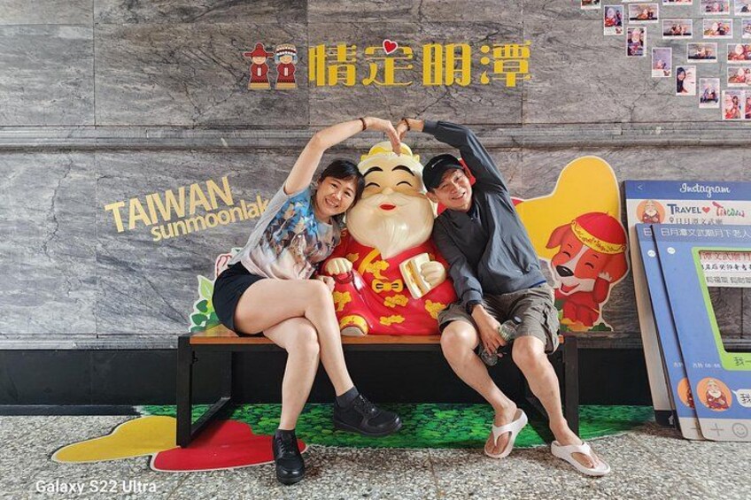 Two people sitting on a bench with a wall in the background displaying the text 'TAIWAN sunmoonlak' and a poster of a dog. 3