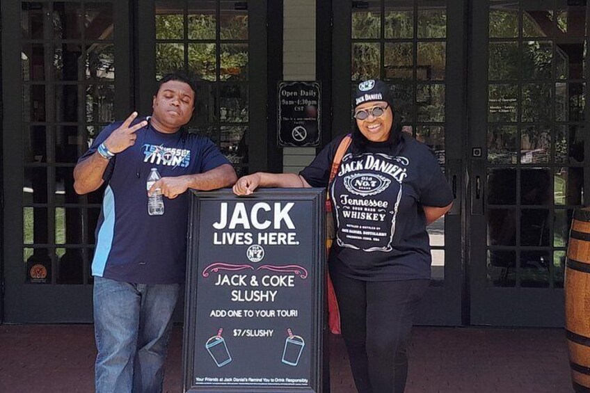 Two people standing in front of a signboard with text and a logo. 3
