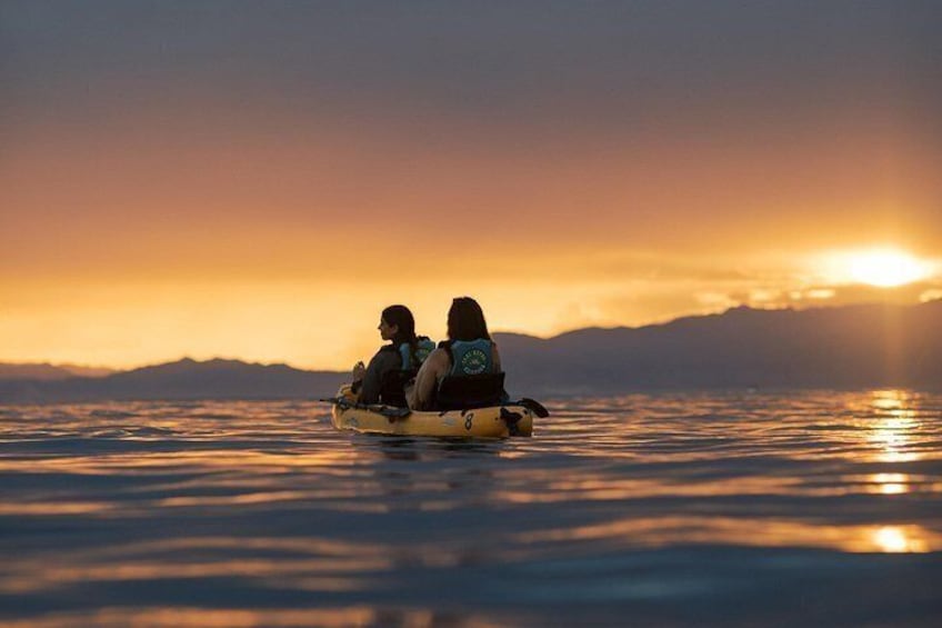 Deux personnes pratiquent le kayak sur une eau calme au coucher du soleil, avec des montagnes en arrière-plan. 1