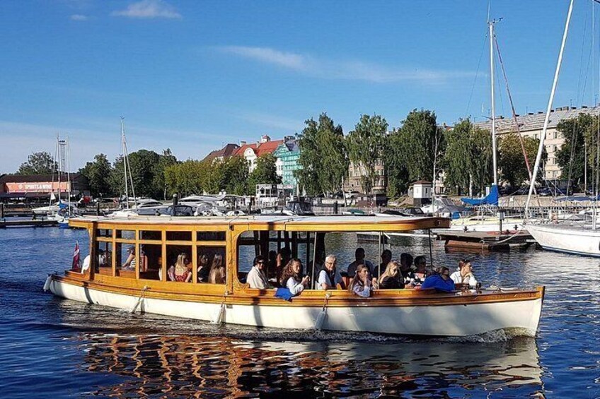 A boat with passengers, docked at a marina with other boats and buildings in the background. 1