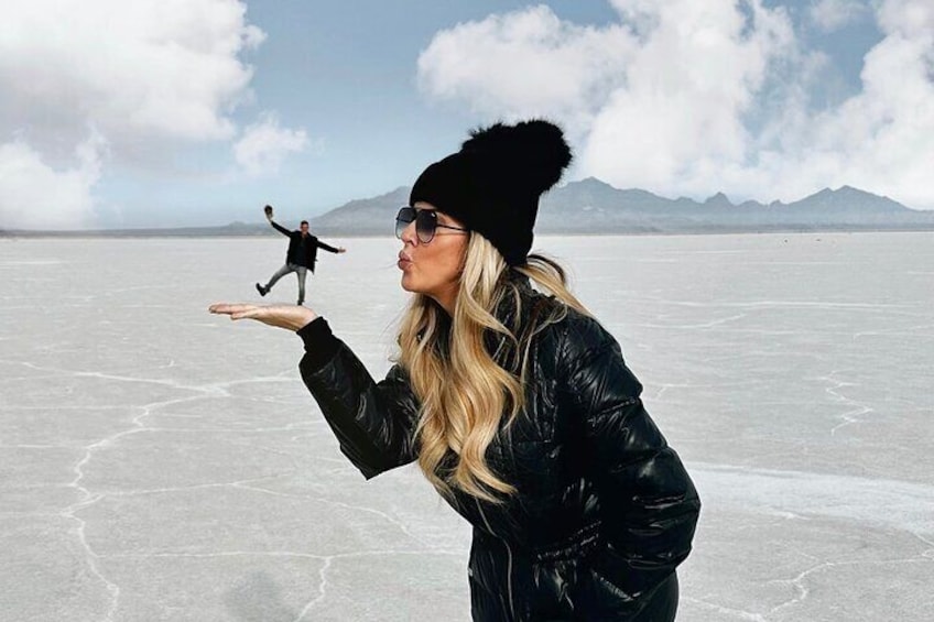 A person in a black jacket and beanie standing on a frozen lake with mountains in the background. 3