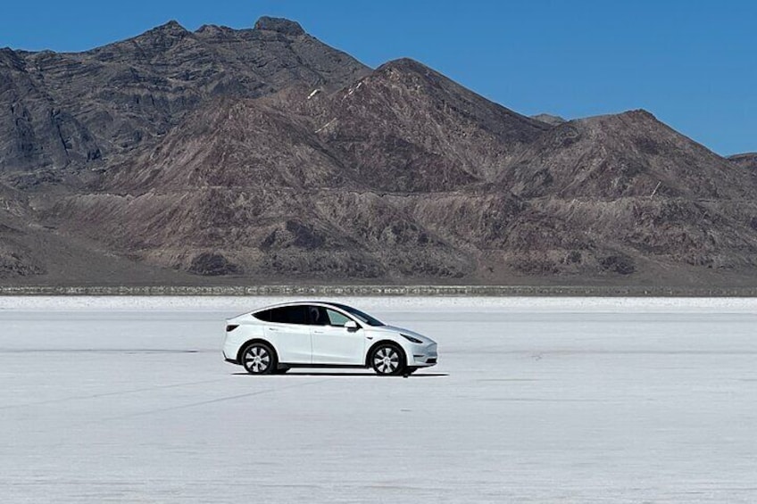 A white car parked on a flat, expansive area with mountains in the background. 1