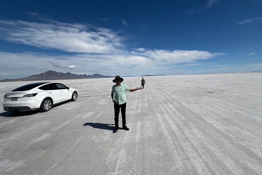 A person standing on a salt flat with a white car and a motorcycle in the background. 2