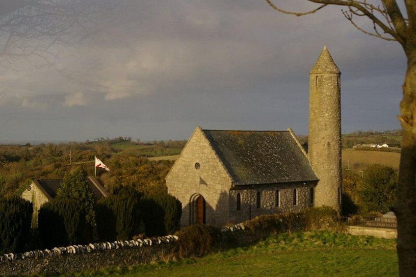 Een stenen kerk met een klokkentoren, omringd door velden en een stenen muur. 4