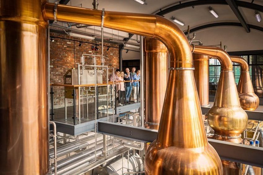 Koperen distillatieapparatuur, een bakstenen muur en mensen die het proces volgen. 1