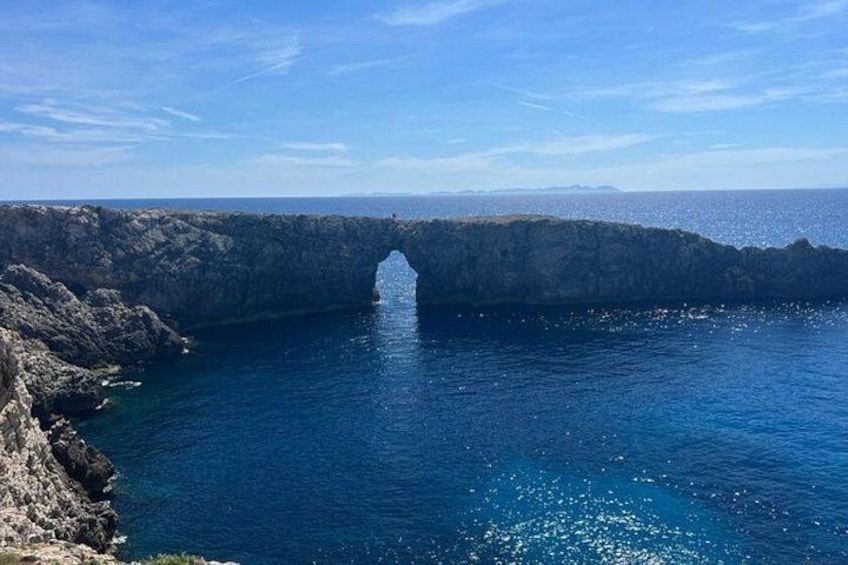 A coastal landscape with a prominent rock formation and a clear blue sea. 2
