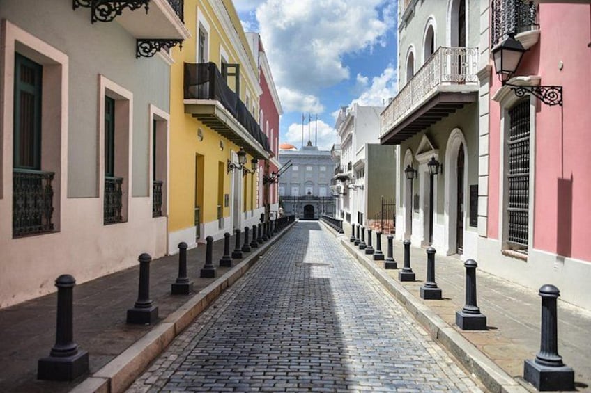 A cobblestone street lined with colorful buildings, black bollards, and a large building in the distance. 2