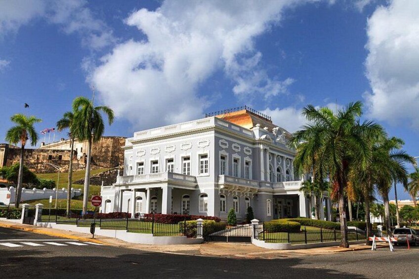 A white colonial-style building with a balcony, palm trees, and a clear blue sky. 3