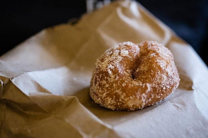 A single sugar-coated doughnut on a piece of brown paper. 4