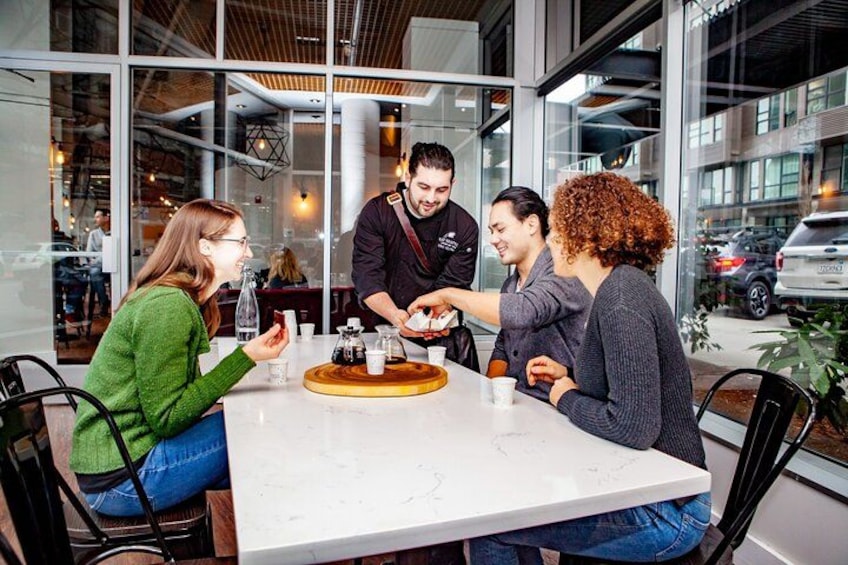 A group of people sitting around a table in a modern indoor setting with large windows. 3