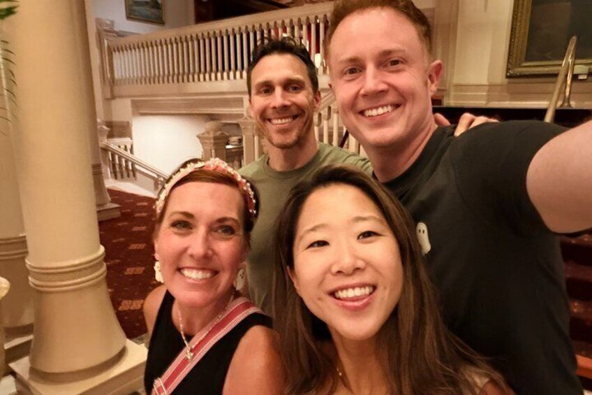 A group of people taking a selfie in a building with a staircase and columns. 2