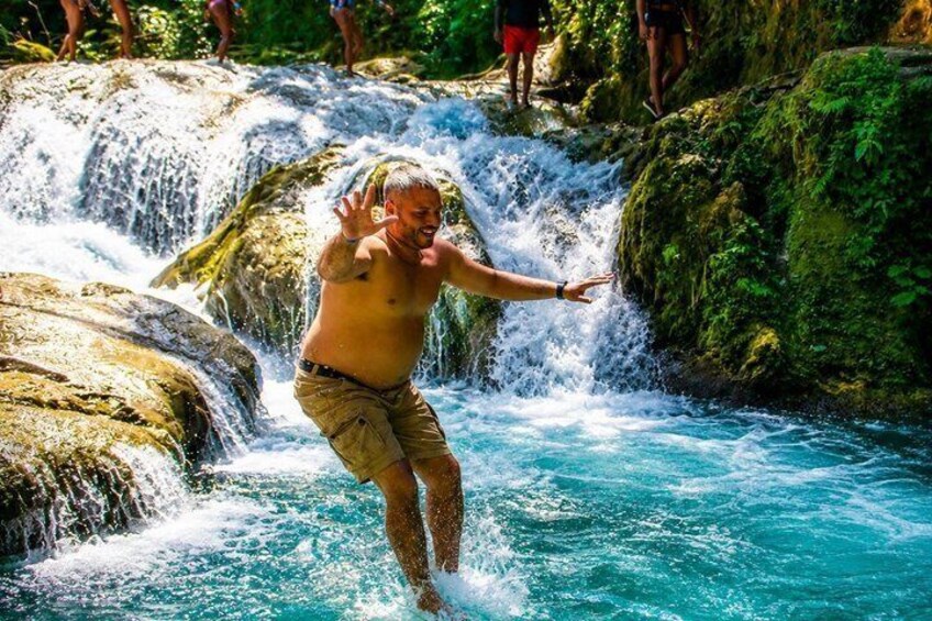 A person jumping into a waterfall surrounded by rocks and greenery. 4