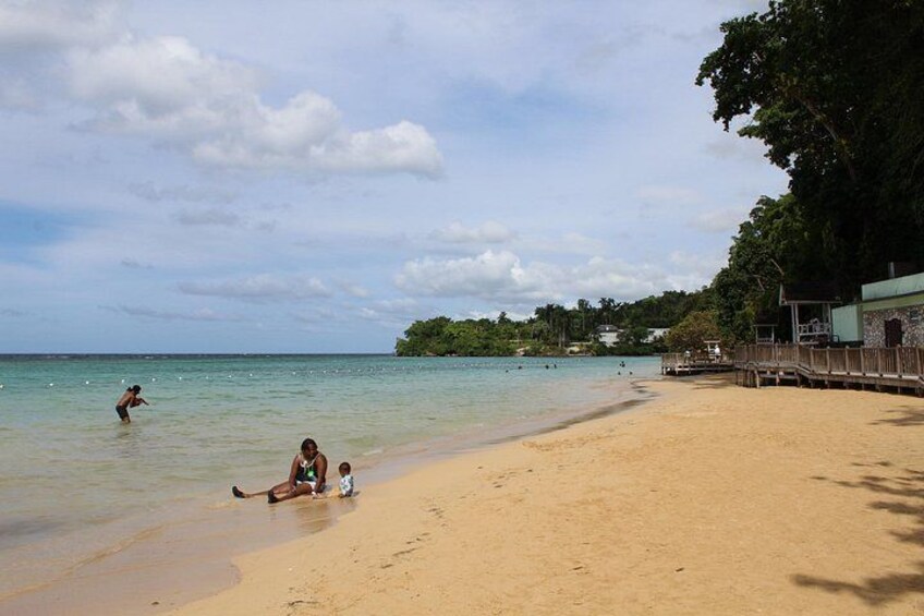 Ein Strand mit Menschen, einer Holzstege und einer bewaldeten Insel in der Ferne. 3