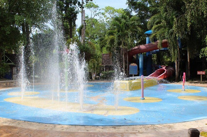 Ein Wasserpark mit einer großen Fontäne, einer roten Rutsche und einem blauen Poolbereich. 4