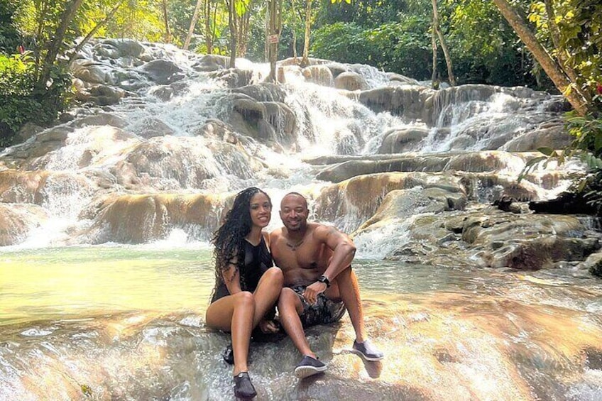 Twee personen zitten op rotsen naast een waterval in een bebost gebied. 4