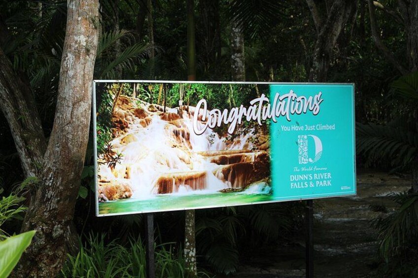 Ein Glückwunschschild mit einem Wasserfall und dem Logo von Dunn's River Falls & Park. 5