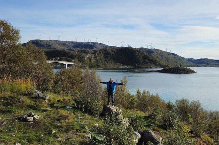 A person standing on a grassy hill overlooking a lake with wind turbines in the background. 4