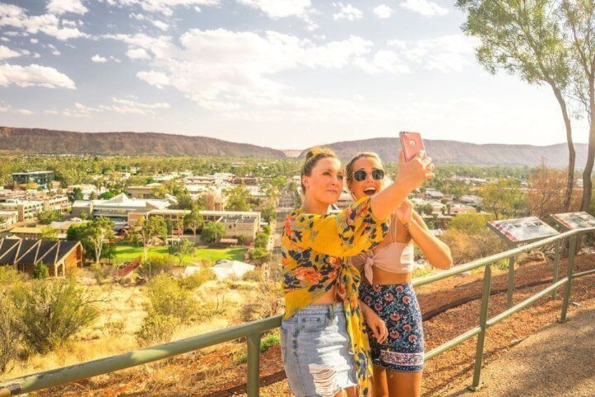 Dos personas tomándose un selfie con una vista panorámica de un pueblo y montañas al fondo. 1