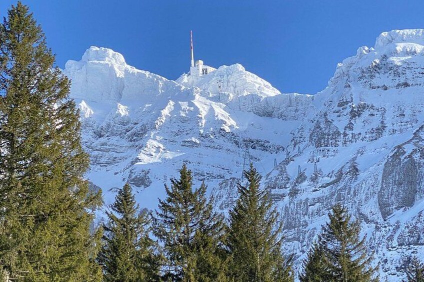 A snow-covered mountain with a tall structure on top, surrounded by evergreen trees. 2