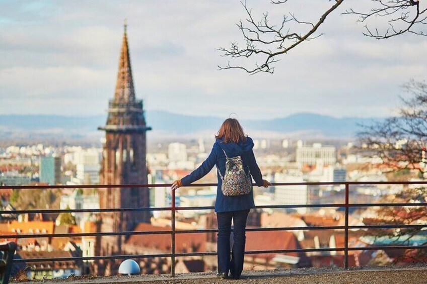 Une personne se tient sur un pont, d’où l’on peut admirer une vue panoramique sur la ville, avec une tour imposante en arrière-plan. 2