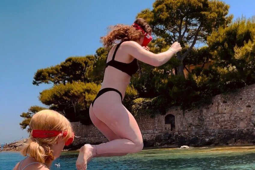 A person jumping into the water from a cliff with trees and a stone wall in the background. 3