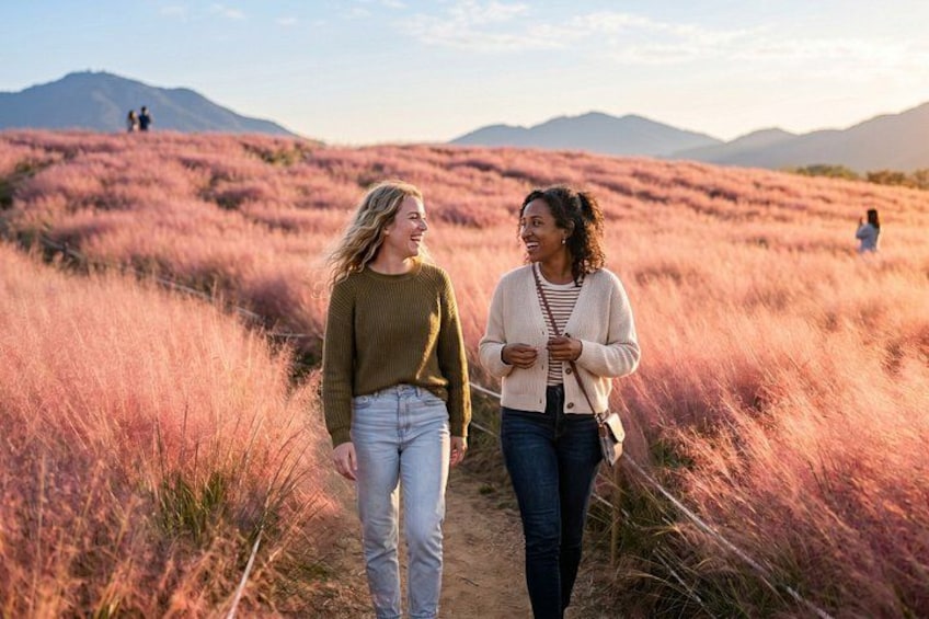 Two people walking on a path in a field with tall grass and mountains in the background. 1