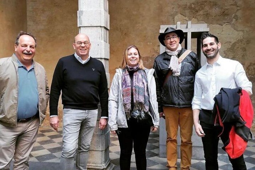 Un grupo de cinco personas de pie frente a un edificio con piso a cuadros y un pilar de piedra. 5