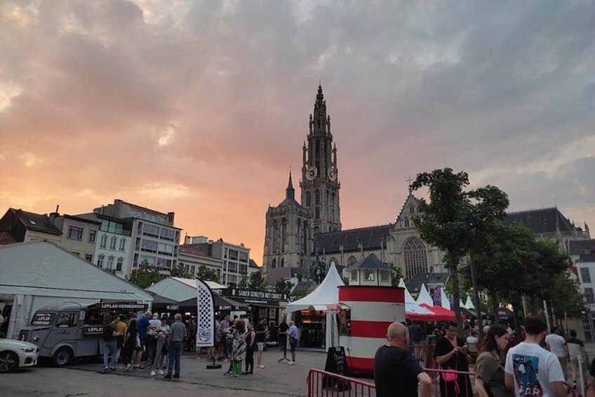 Une place de ville avec un clocher d’église imposant, des étals de marché et une foule de personnes rassemblées autour. 1