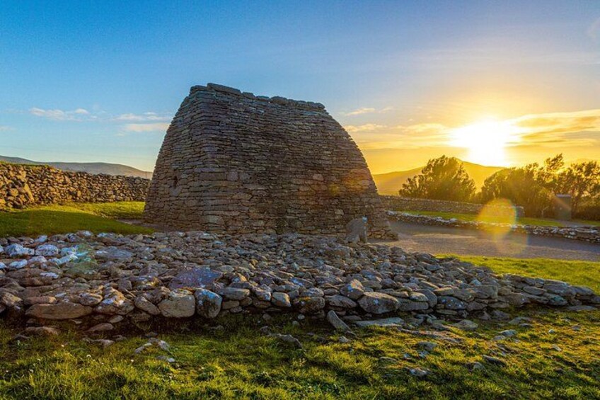 Una estructura de piedra en un campo con césped, con un atardecer de fondo. 1