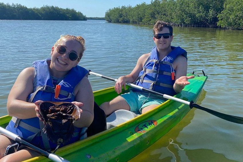 Two people in a green canoe on a calm body of water with trees in the background. 4