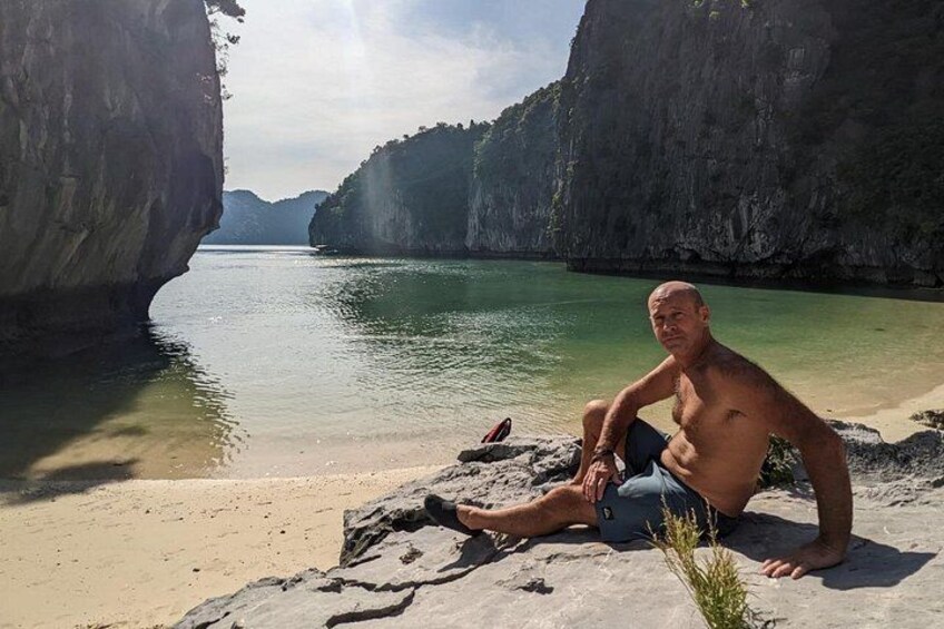 Un hombre sentado sobre una roca frente a un mar tranquilo, con acantilados al fondo. 3