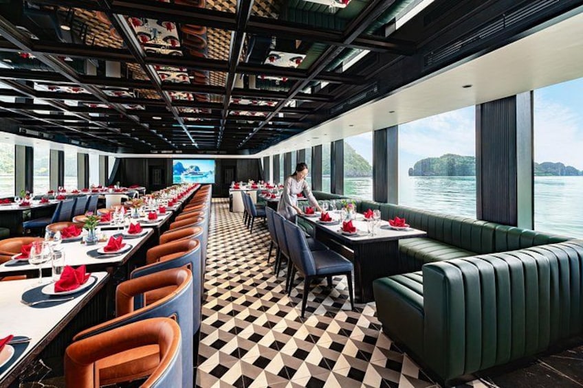 Een restaurant met gedekte tafels, een bedienend personeelslid en uitzicht op water en heuvels. 3