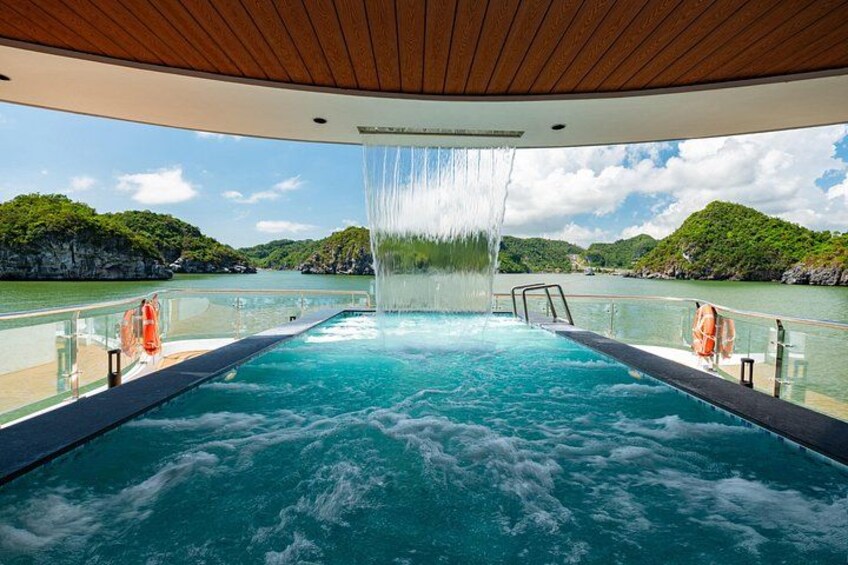 Une piscine agrémentée d’une cascade, entourée d’une terrasse en bois et d’une balustrade, offrant une vue sur une étendue d’eau et une végétation luxuriante en arrière-plan. 2