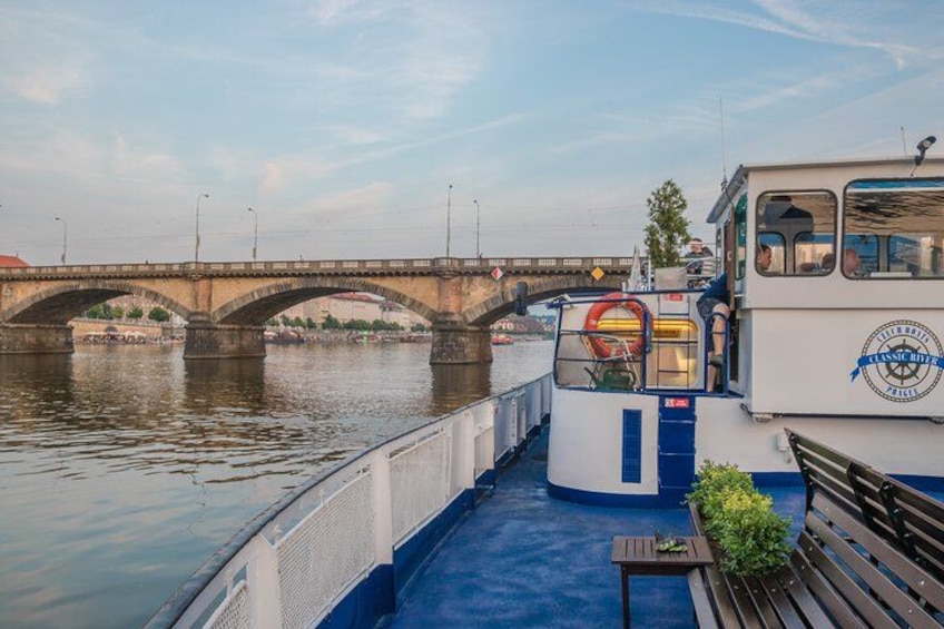 A river with a bridge, a boat with a blue deck, and a bench. 2