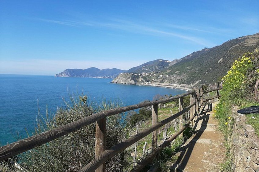 Un sendero costero con barandilla de madera, con vistas al mar y un paisaje montañoso. 3